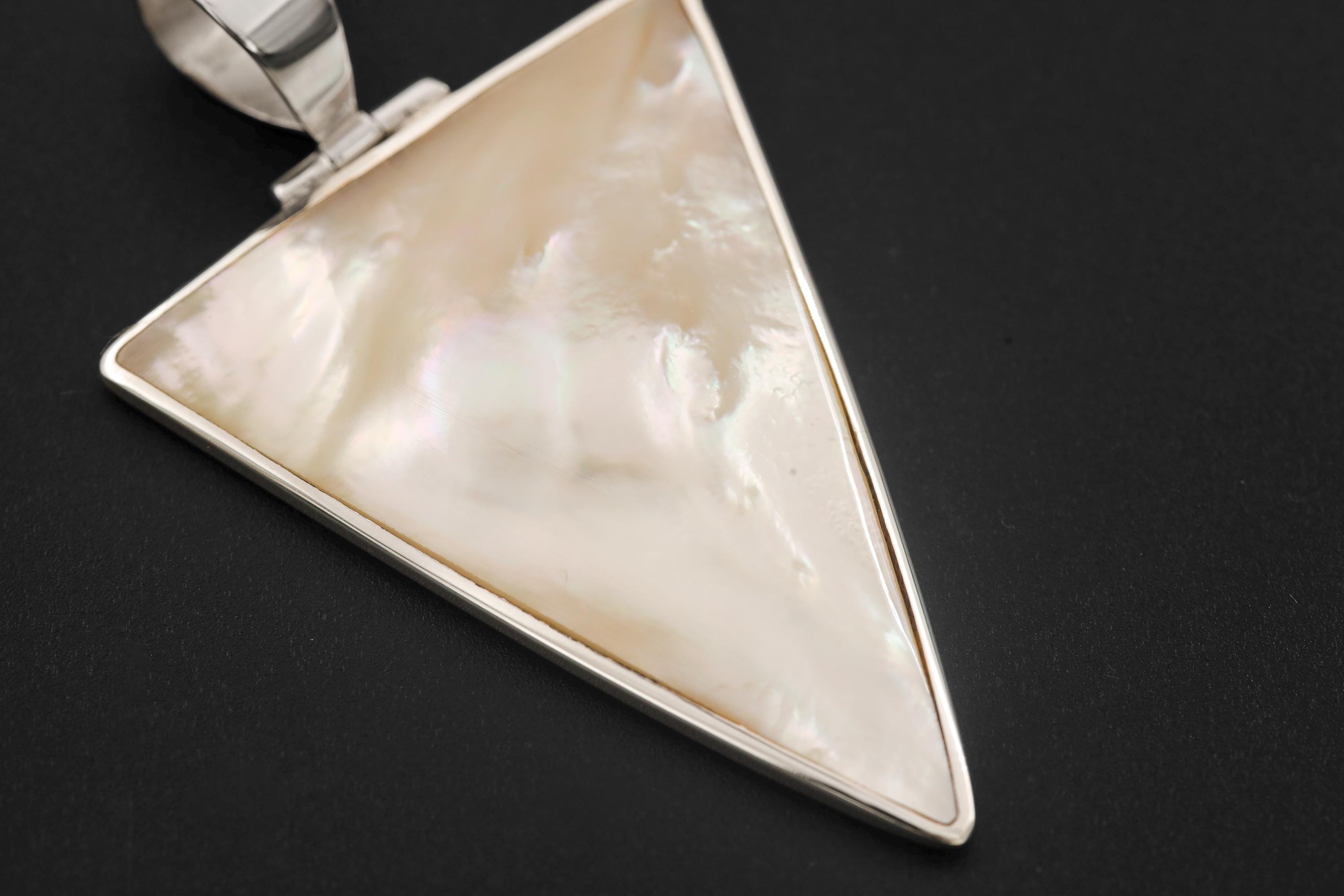 Mother of Pearl triangle pendant displayed on dark background with silver chain and geometric shell design.