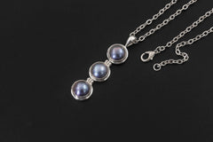 Black Pearl pendant displayed on dark background with sterling silver chain and vertical triple pearl design.