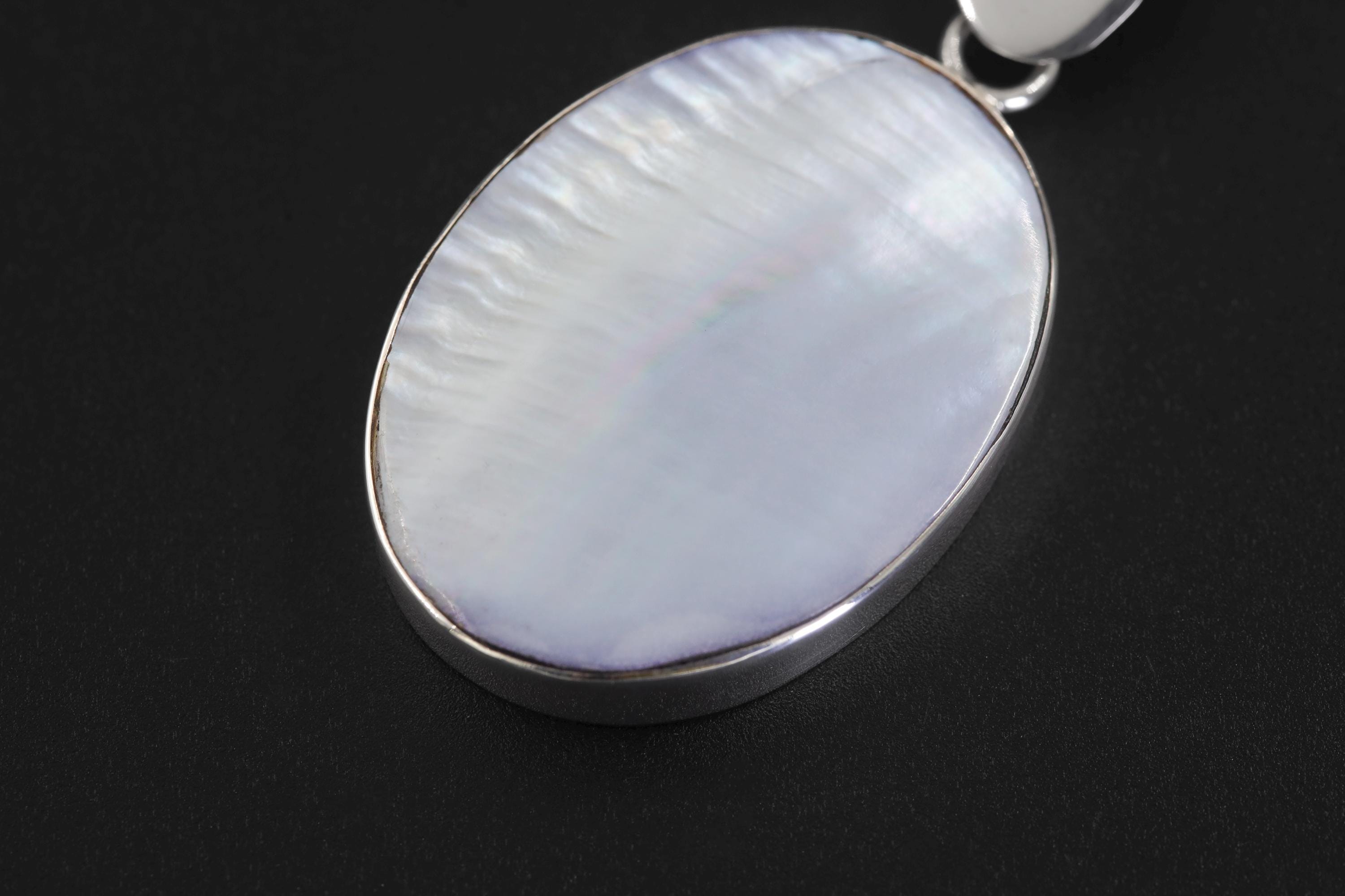Close view of Mother of Pearl pendant showing rainbow nacre reflection and triangular silver bail.