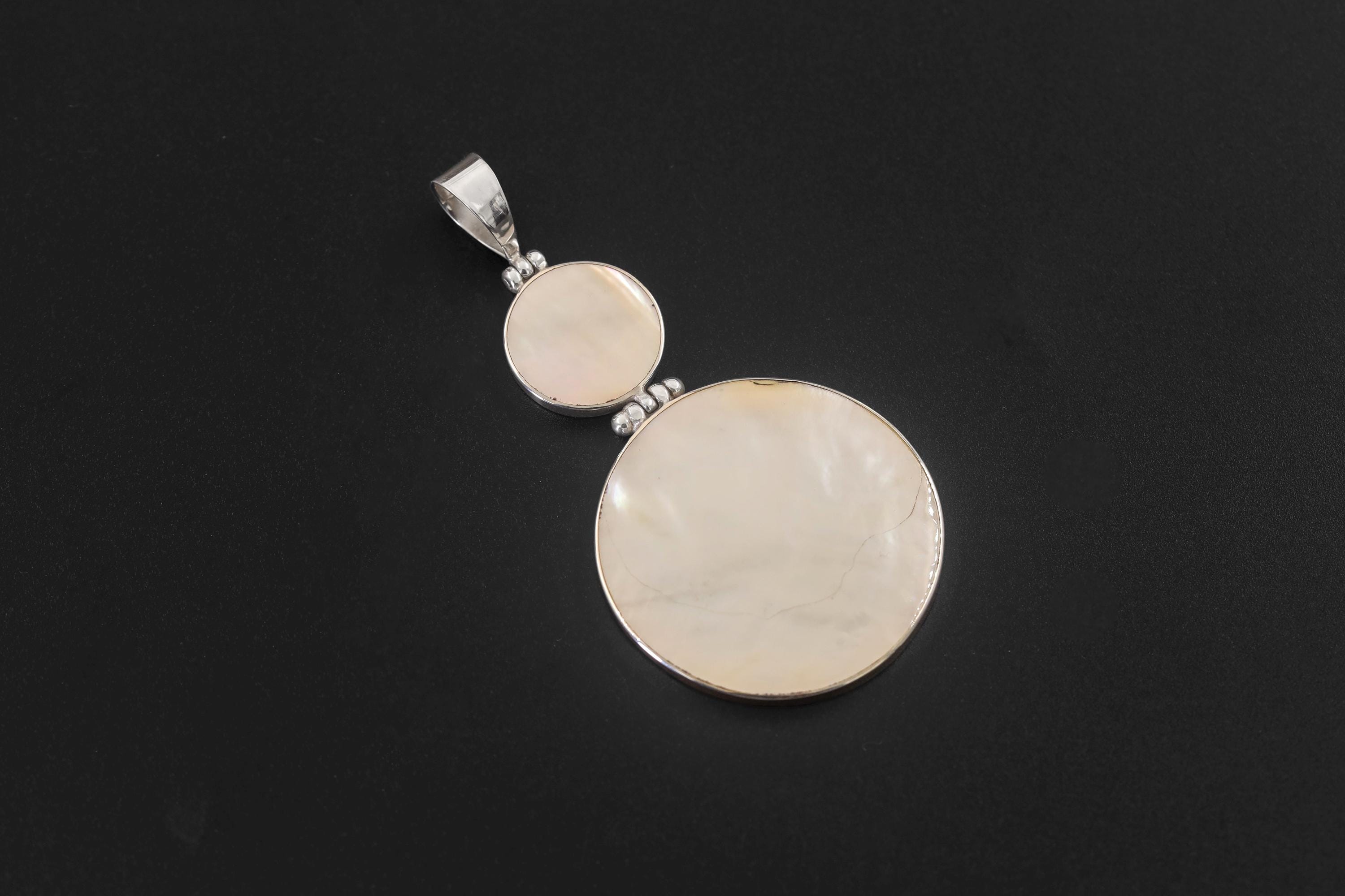 Mother of Pearl double disc pendant shown on natural wood with polished sterling silver bezel settings.