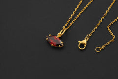 Garnet marquise pendant shown with gold-plated chain on dark background as a petite red gemstone charm.