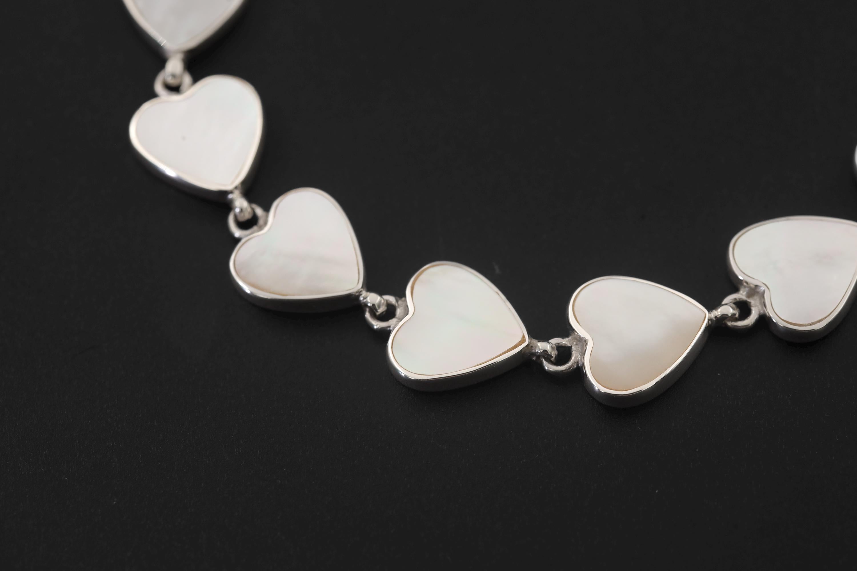 Close view of Mother of Pearl heart bracelet showing white shell cabochons in polished silver bezels.