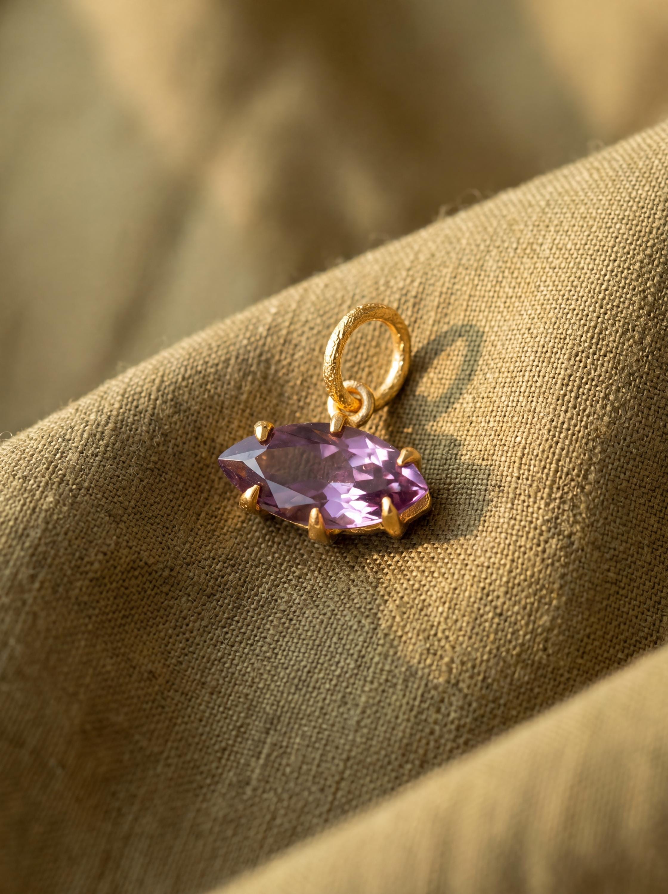 Amethyst eye pendant displayed on warm fabric with gold-plated sterling silver and violet marquise stone.