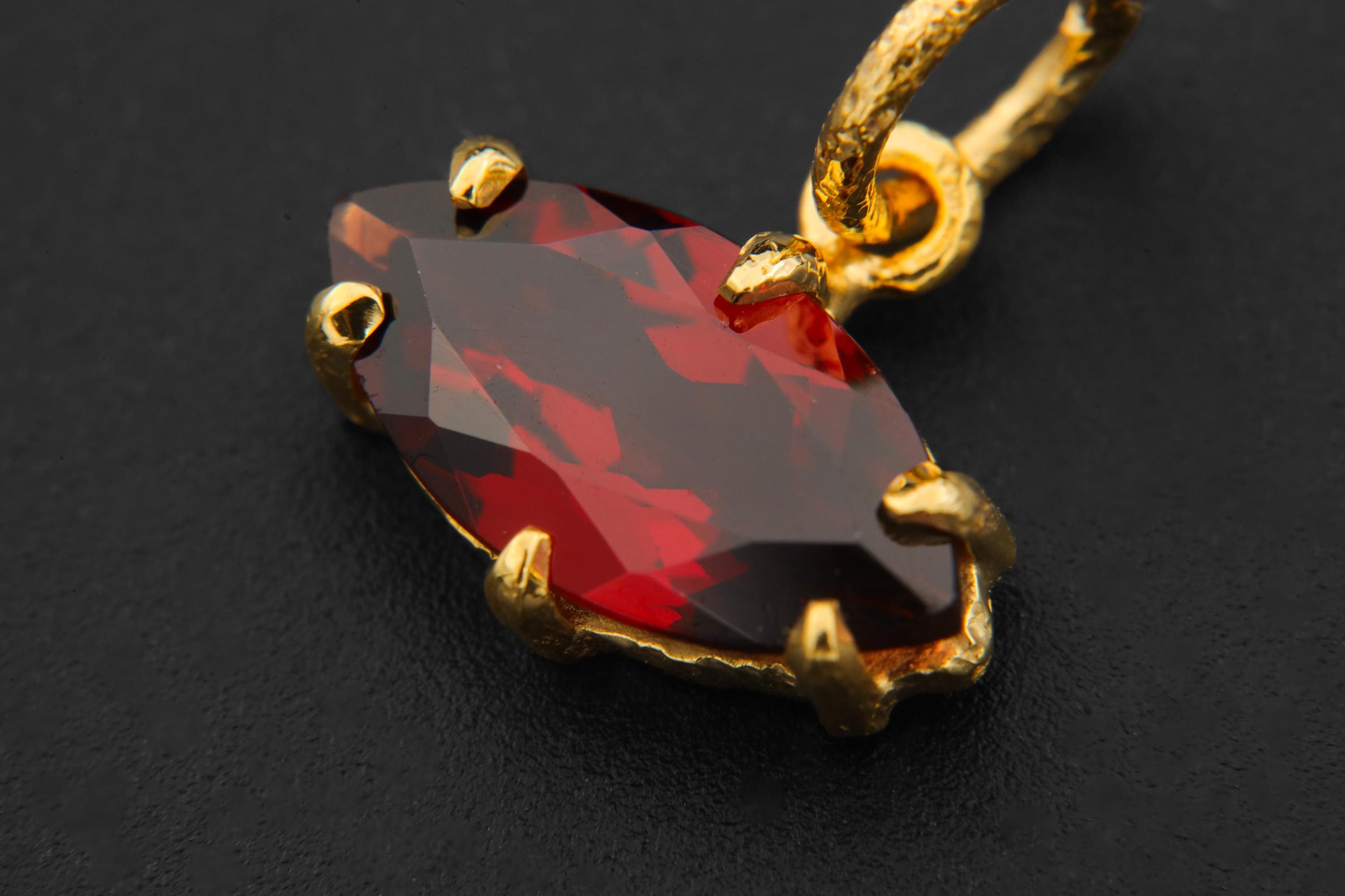 Garnet pendant displayed on dark background with gold-plated sterling silver bail and claw setting.