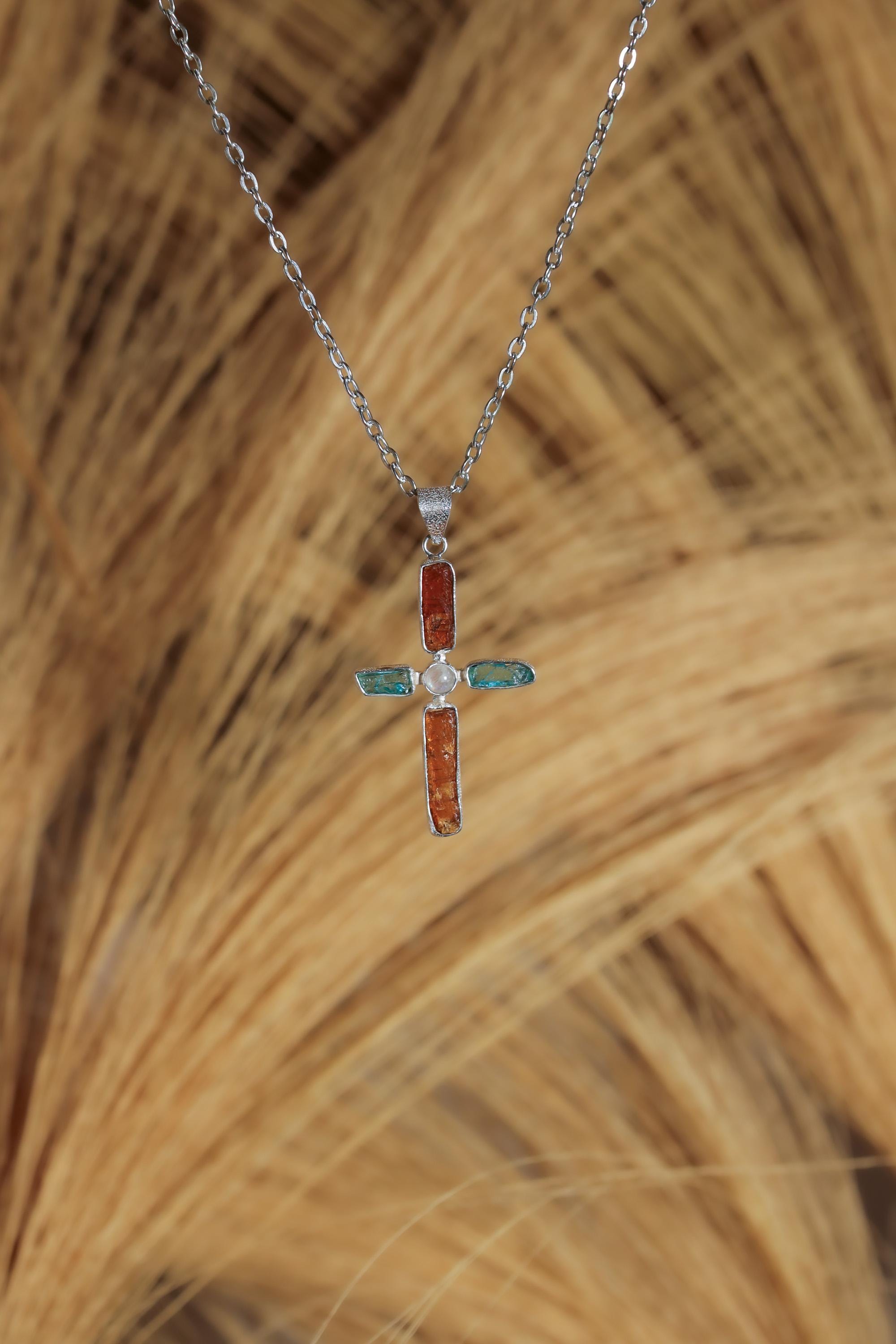 Celestial Harmony Cross pendant shown on a natural background with Red Kyanite, Apatite, Moonstone, and sterling silver setting.