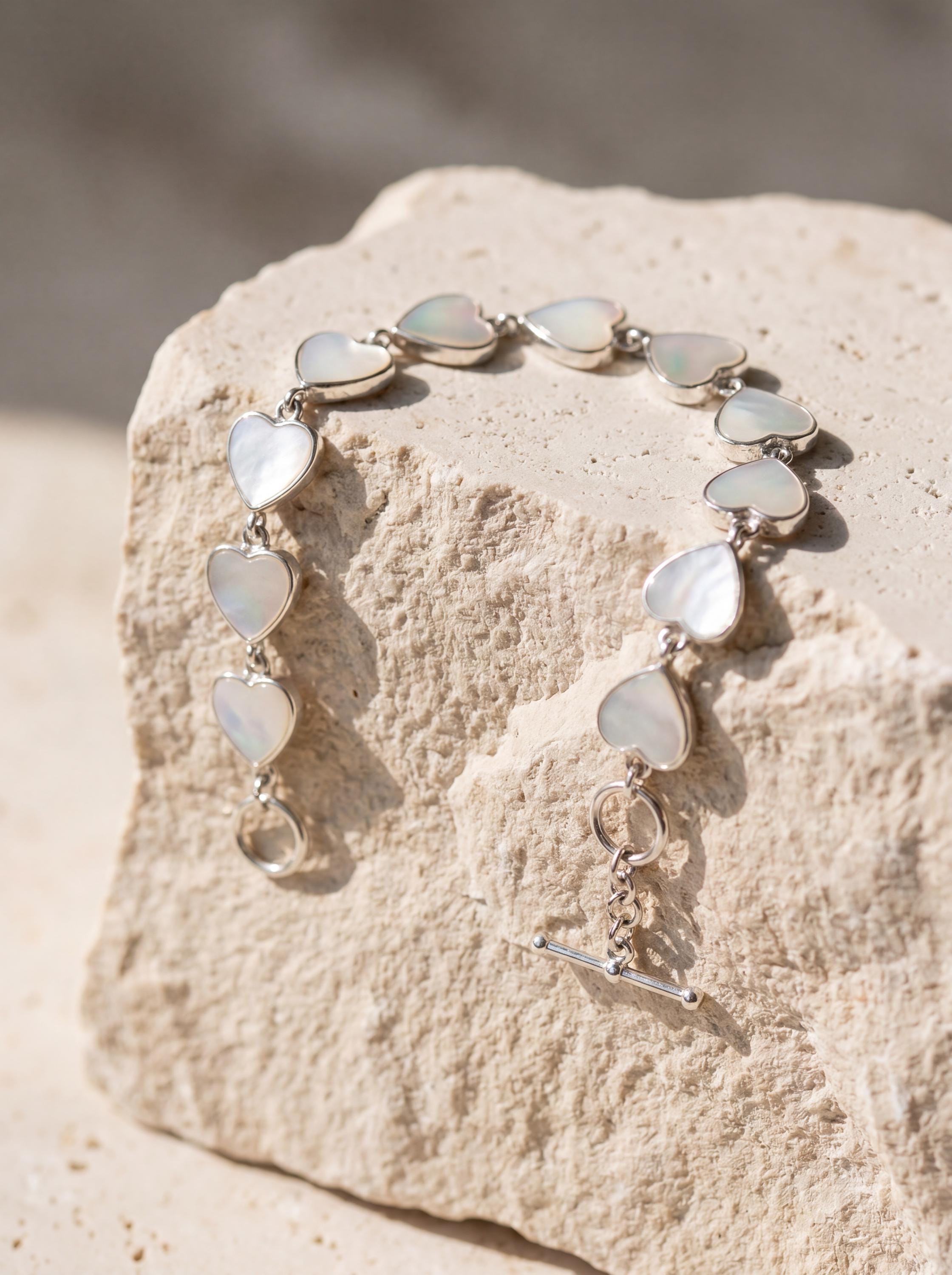 Mother of Pearl heart bracelet shown on textured stone with polished sterling silver settings and toggle clasp.