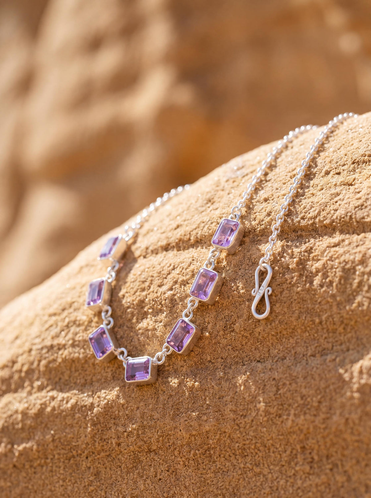 Amethyst sterling silver necklace shown on sand with seven square purple gemstones and fine silver chain.