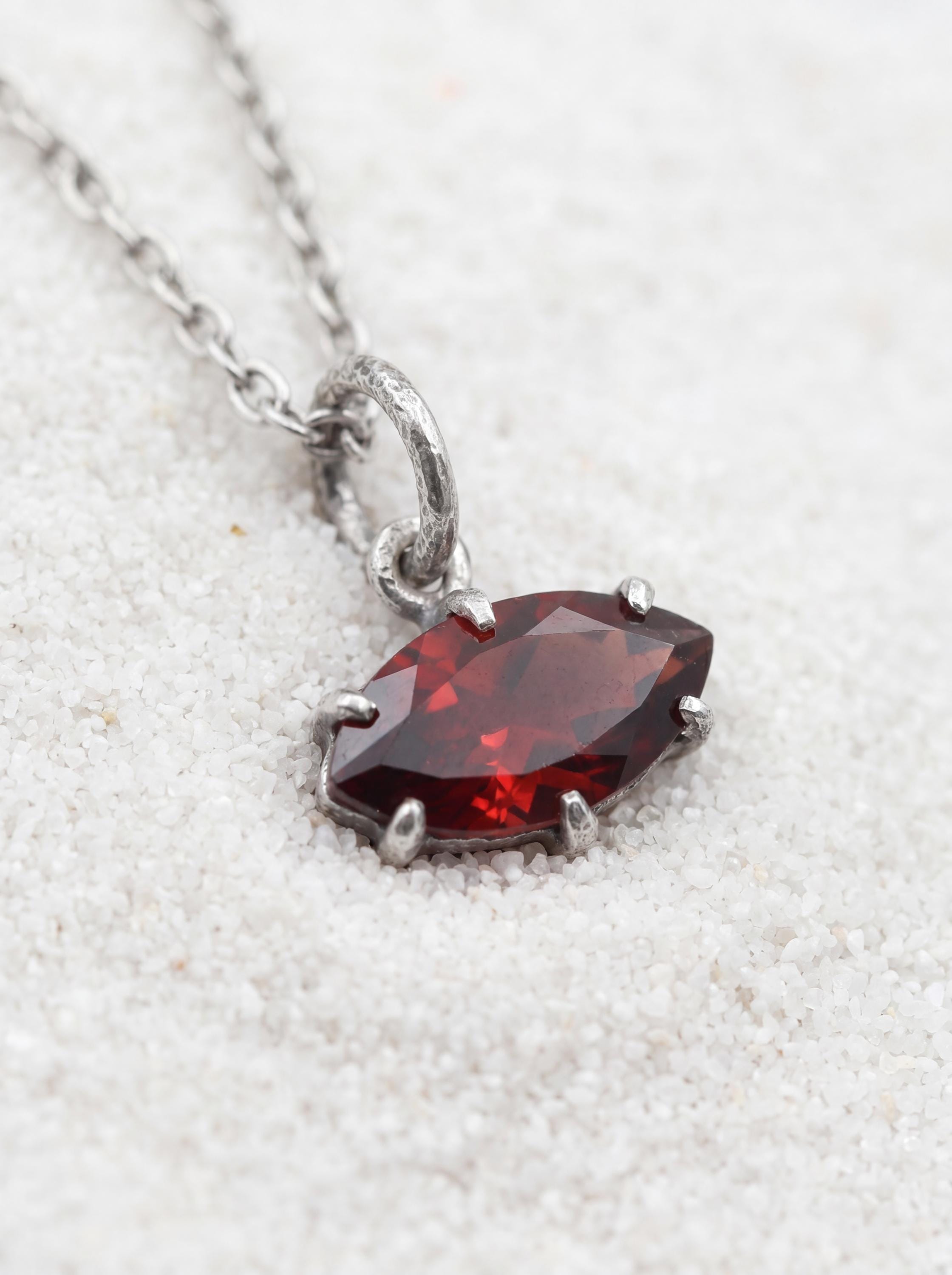 Faceted Garnet marquise pendant shown on light fabric with sterling silver claw setting.