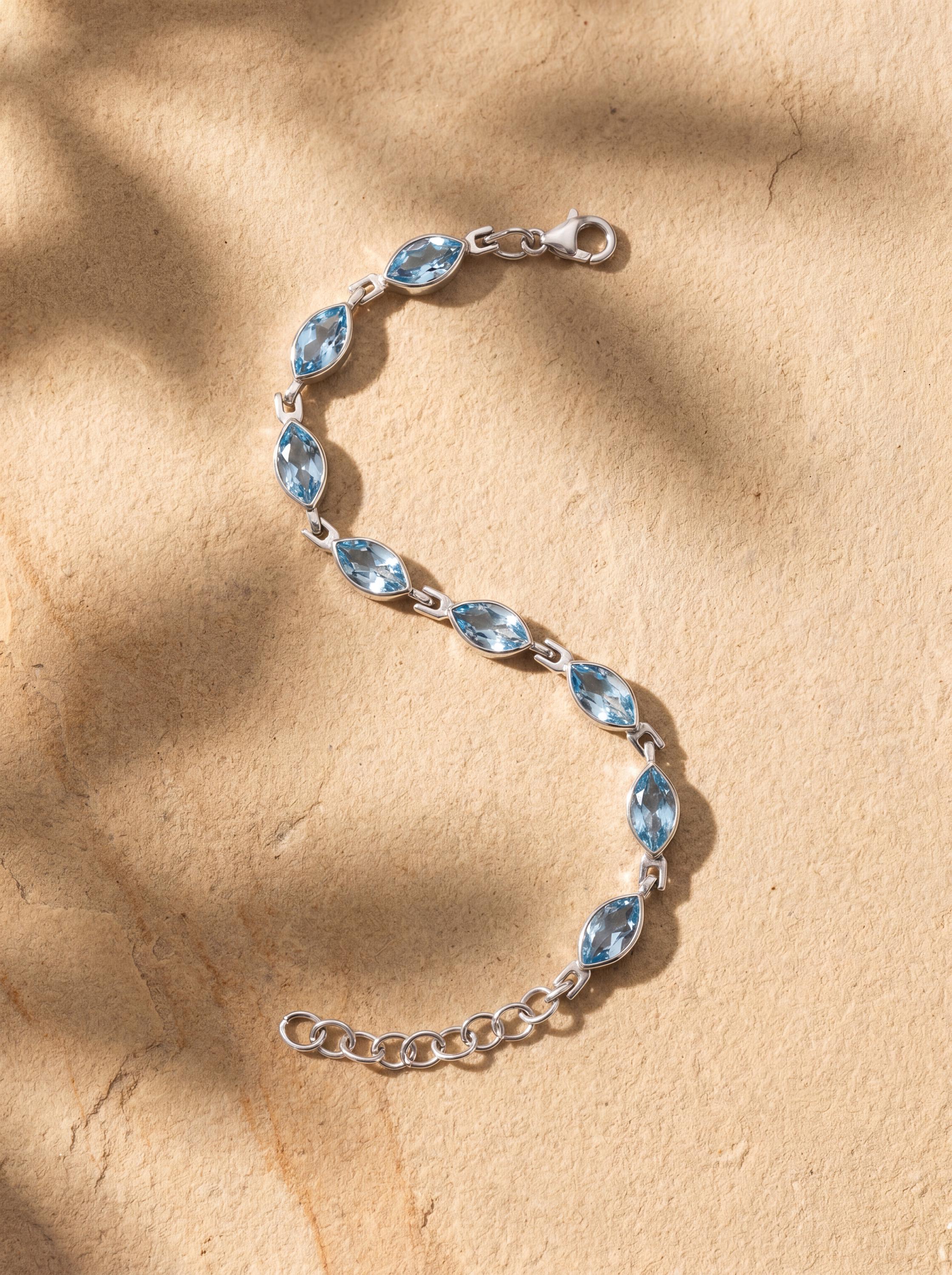 Blue Topaz bracelet shown on sand with light blue gemstone sparkle and polished sterling silver settings.