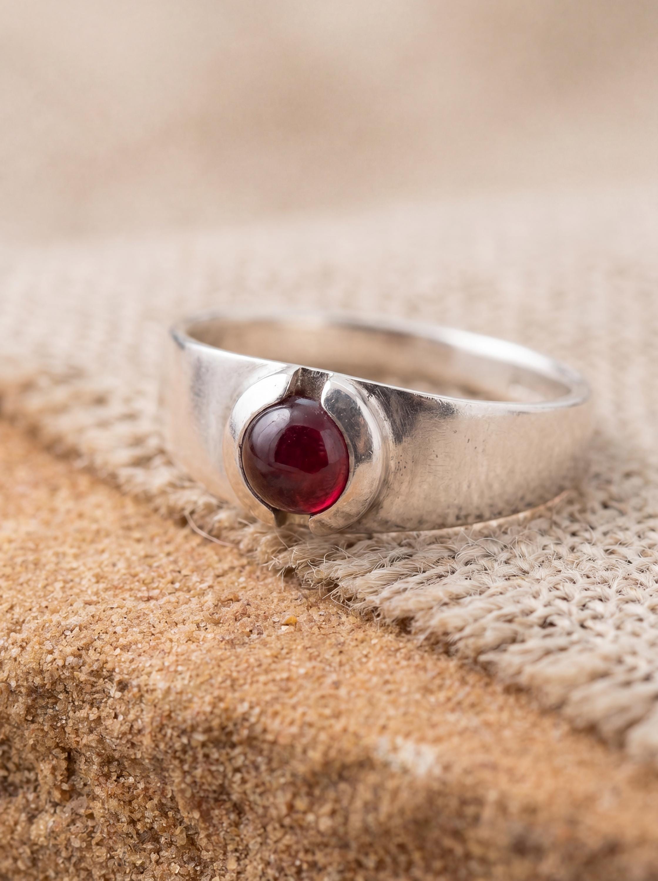 Garnet cabochon ring displayed on warm fabric with high-shine sterling silver band.