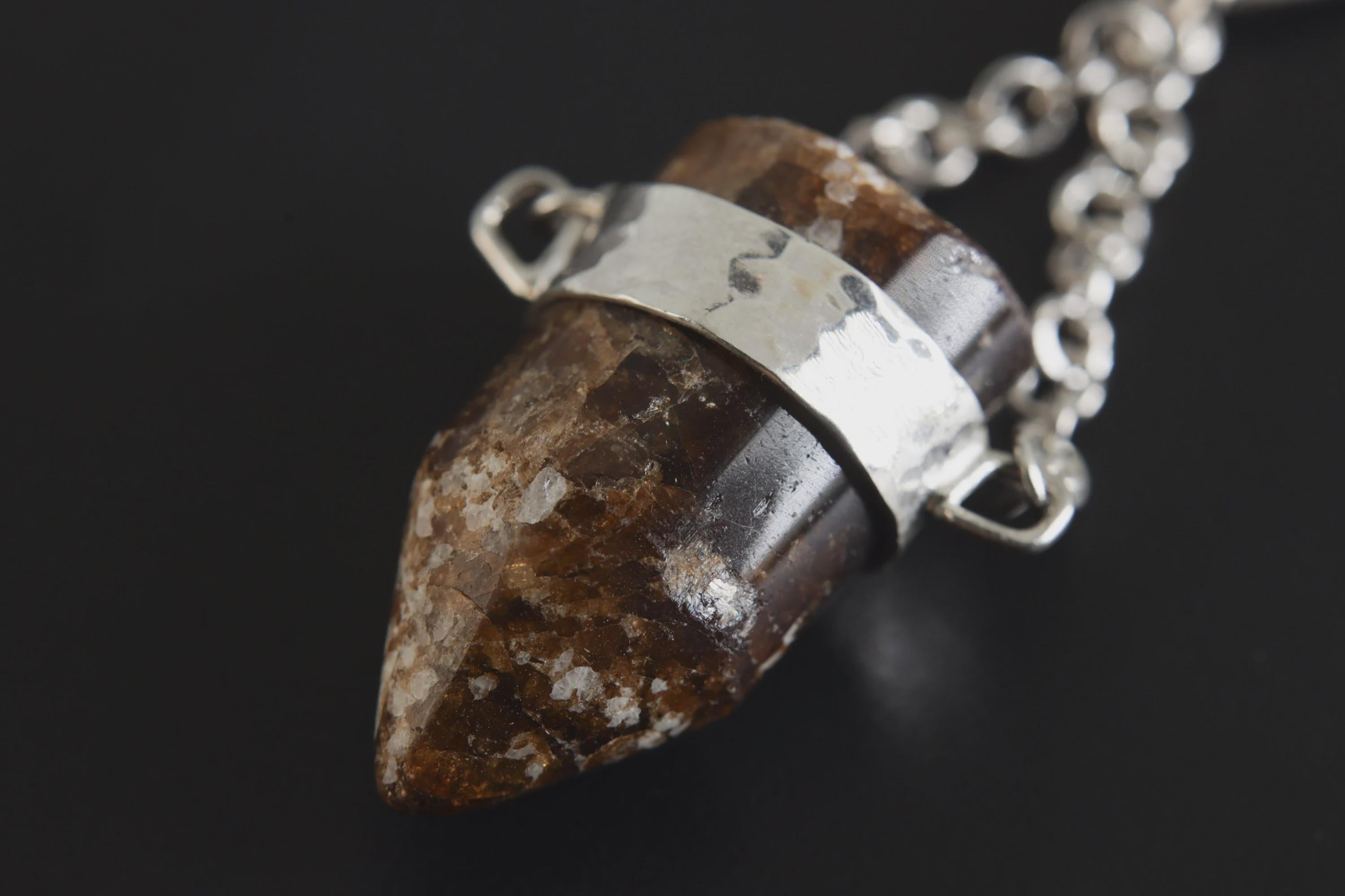 Close-up of bullet-shaped Brown Tourmaline Dravite showing deep earthy colour and hammered sterling silver frame.
